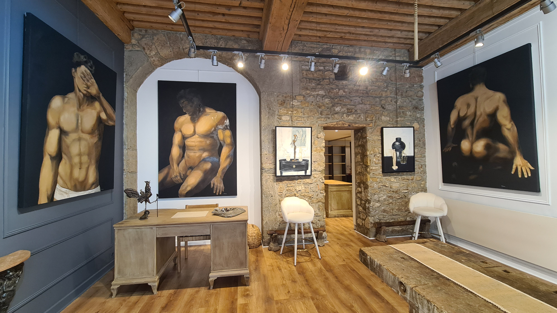 Œuvres accrochées entre mur de pierre et cloison sombre